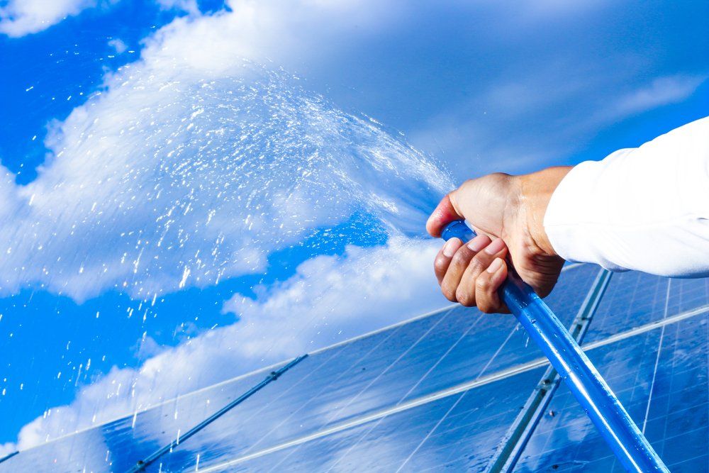 Man Spraying Water on the Dirty Solar Panels — Highlands Window Cleaning in Mittagong, NSW