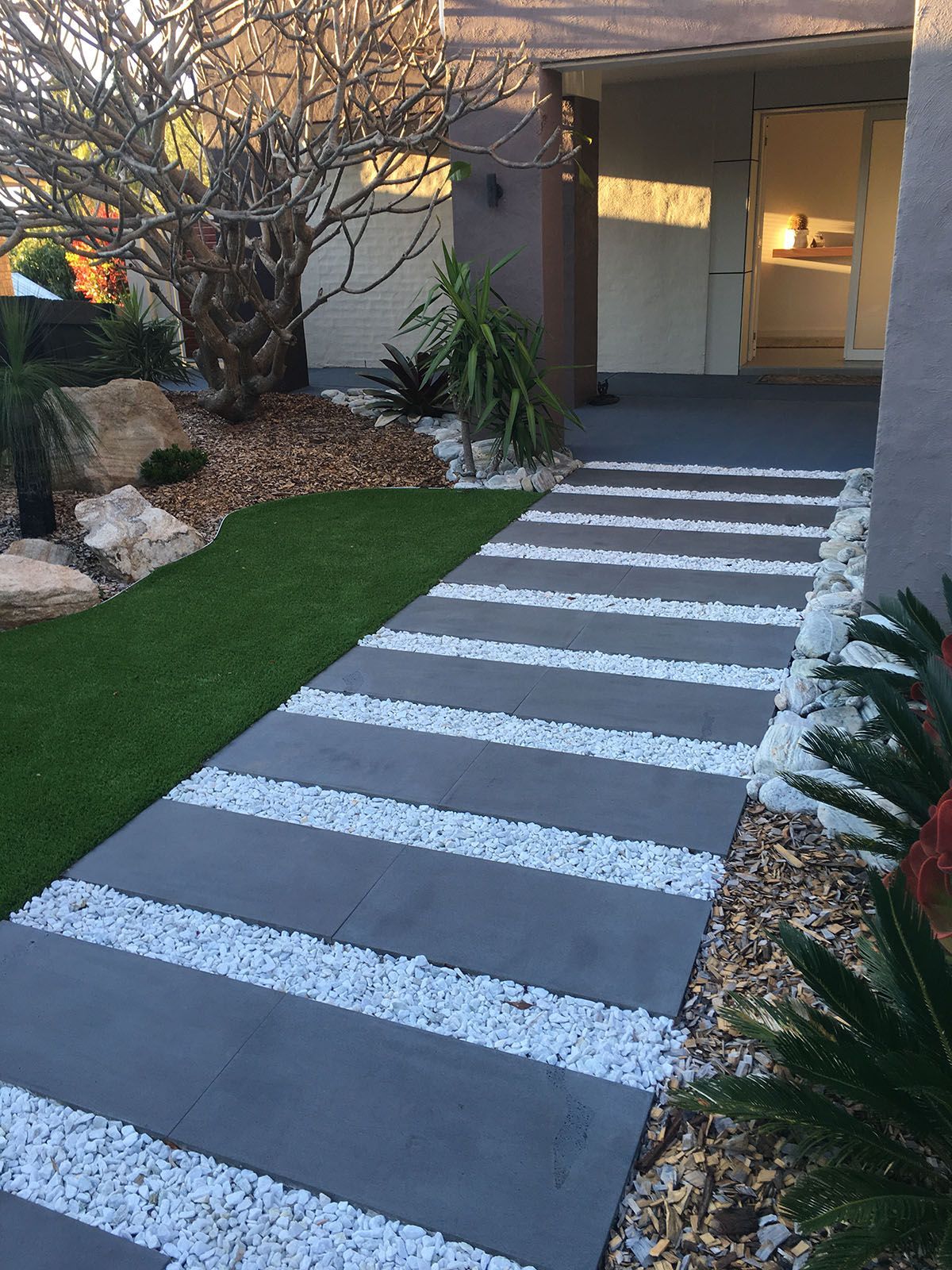 A walkway with white gravel and grass leading to a house.