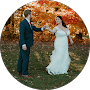 A couple in formal wedding attire dancing outdoors against a backdrop of vibrant orange autumn trees.