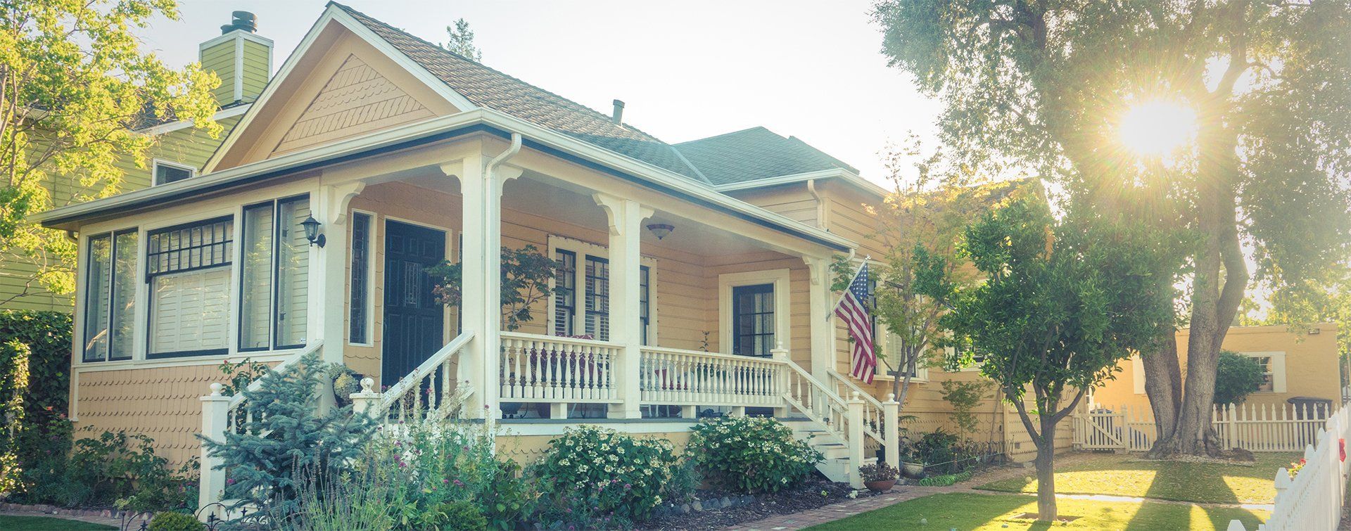 Yellow house with a porch and American flag on a sunny day.