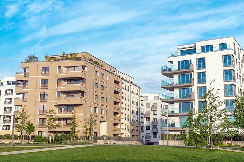 Apartment buildings, tan and white exteriors, balconies, blue sky, green grass.