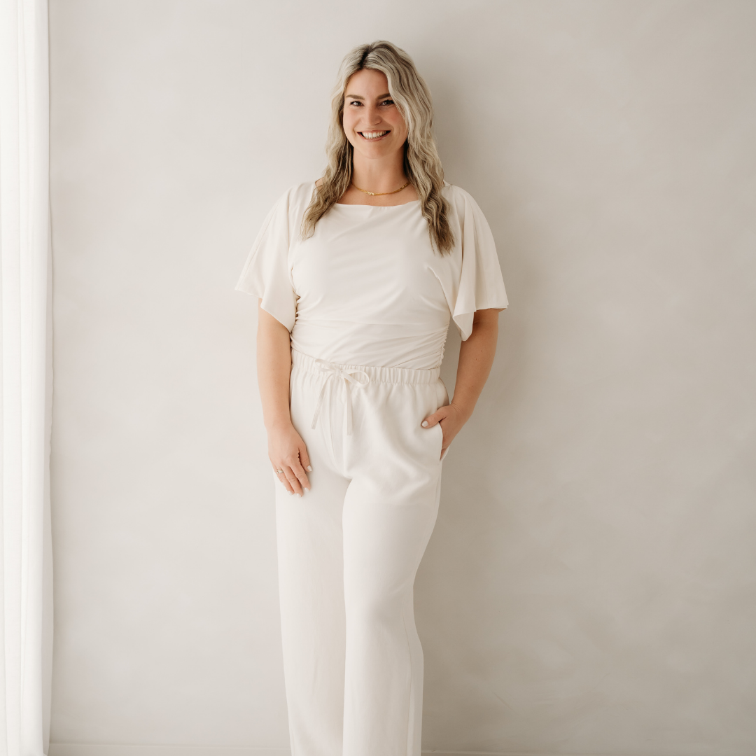 Woman in a white outfit standing against a plain light wall