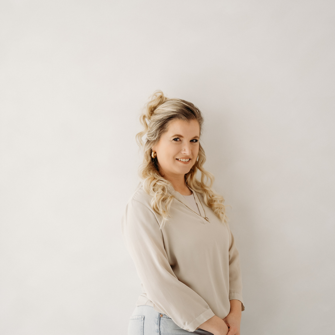 Smiling woman in a beige blouse standing against a plain light background