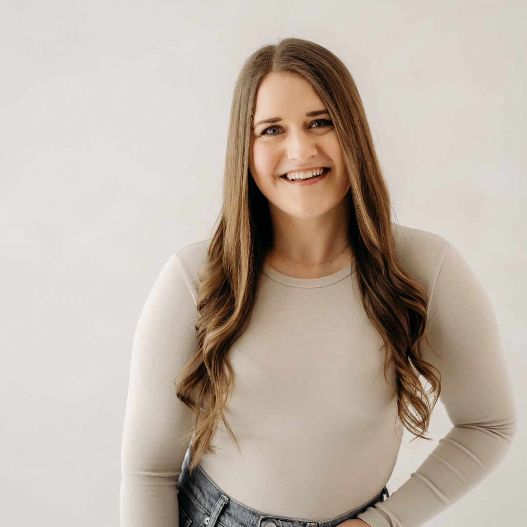 Smiling woman in a light beige top and jeans against a plain background