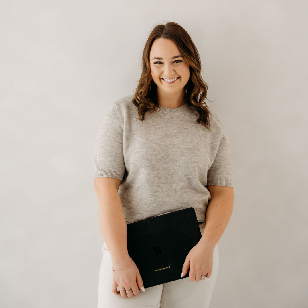 Smiling woman in a beige sweater holding a black laptop against a white background