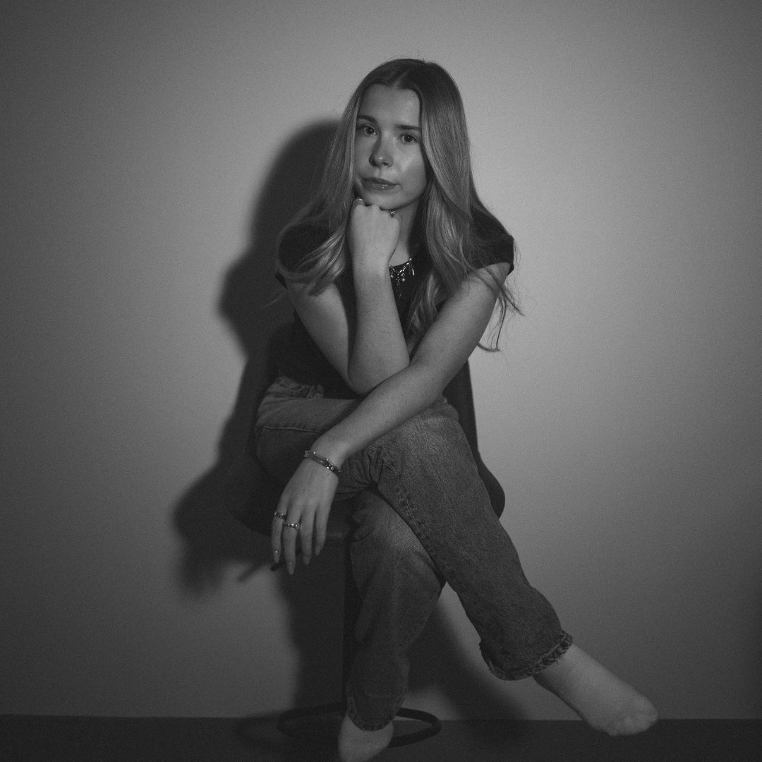 Woman sitting on a chair, leaning forward with crossed legs in a dimly lit room