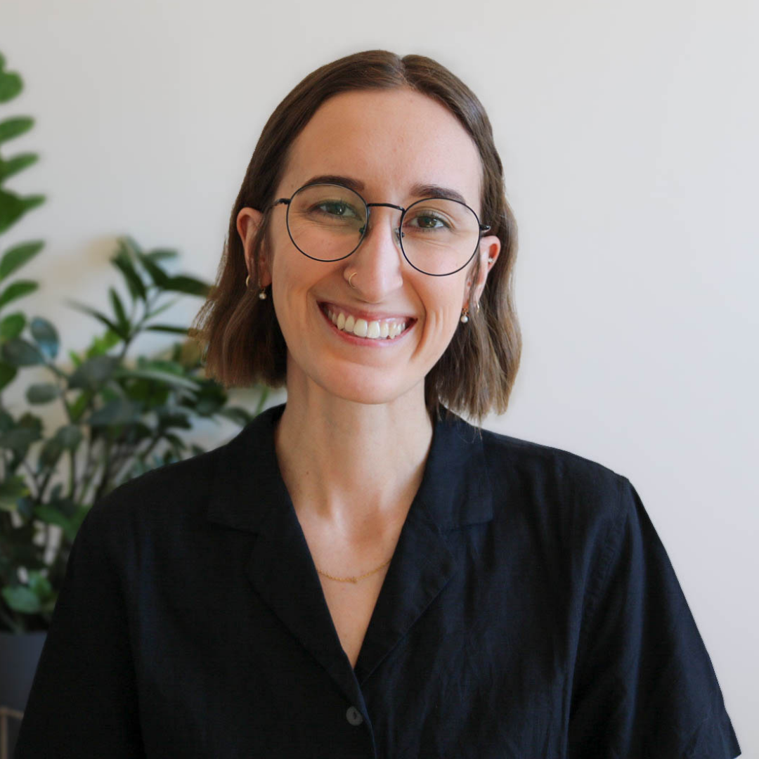 Smiling person in glasses and black shirt indoors, with a plant in the background