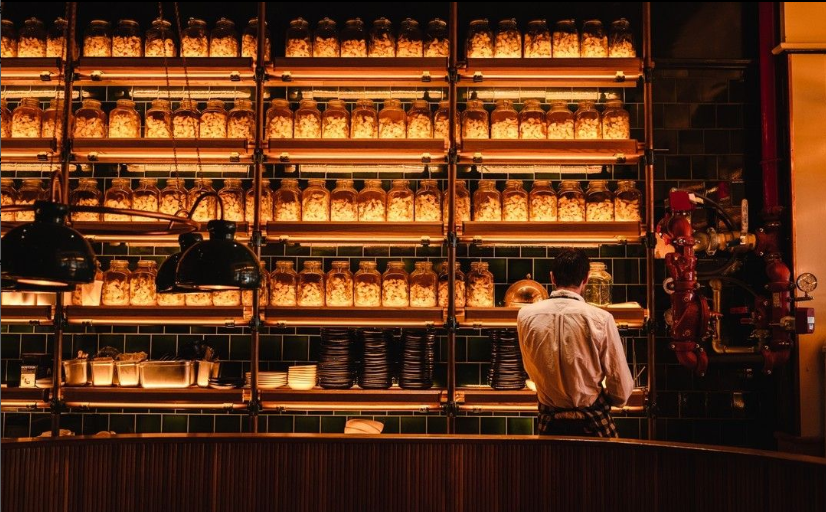 A man standing at a bar in front of a wall of jars