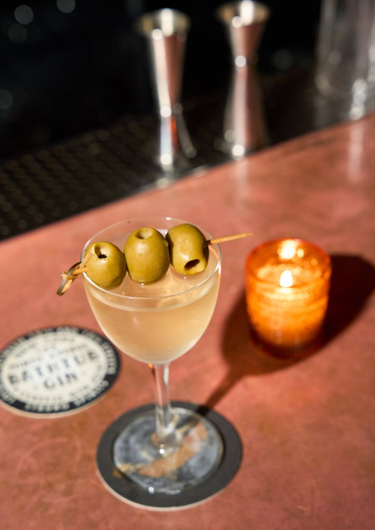 A martini with olives and a candle on a bar