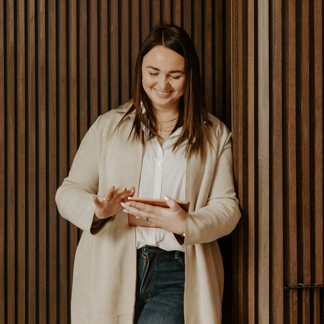 A woman leaning against a wooden wall holding a cell phone
