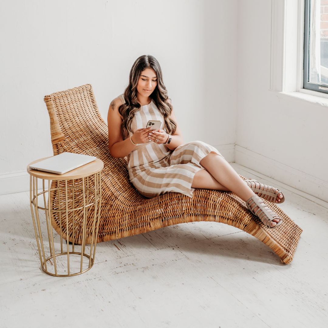 A woman is sitting on a wicker chair looking at her phone.