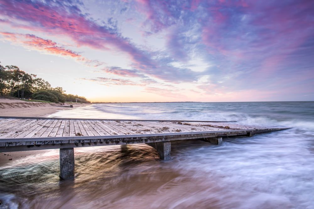 A Wooden Pier Leading to the Ocean at Sunset — Brett Negus Plumbing In Hervey Bay, QLD
