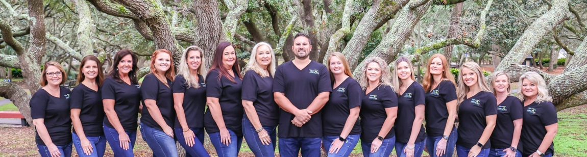 A group of people in black shirts and jeans posing outdoors in front of a flowering tree.