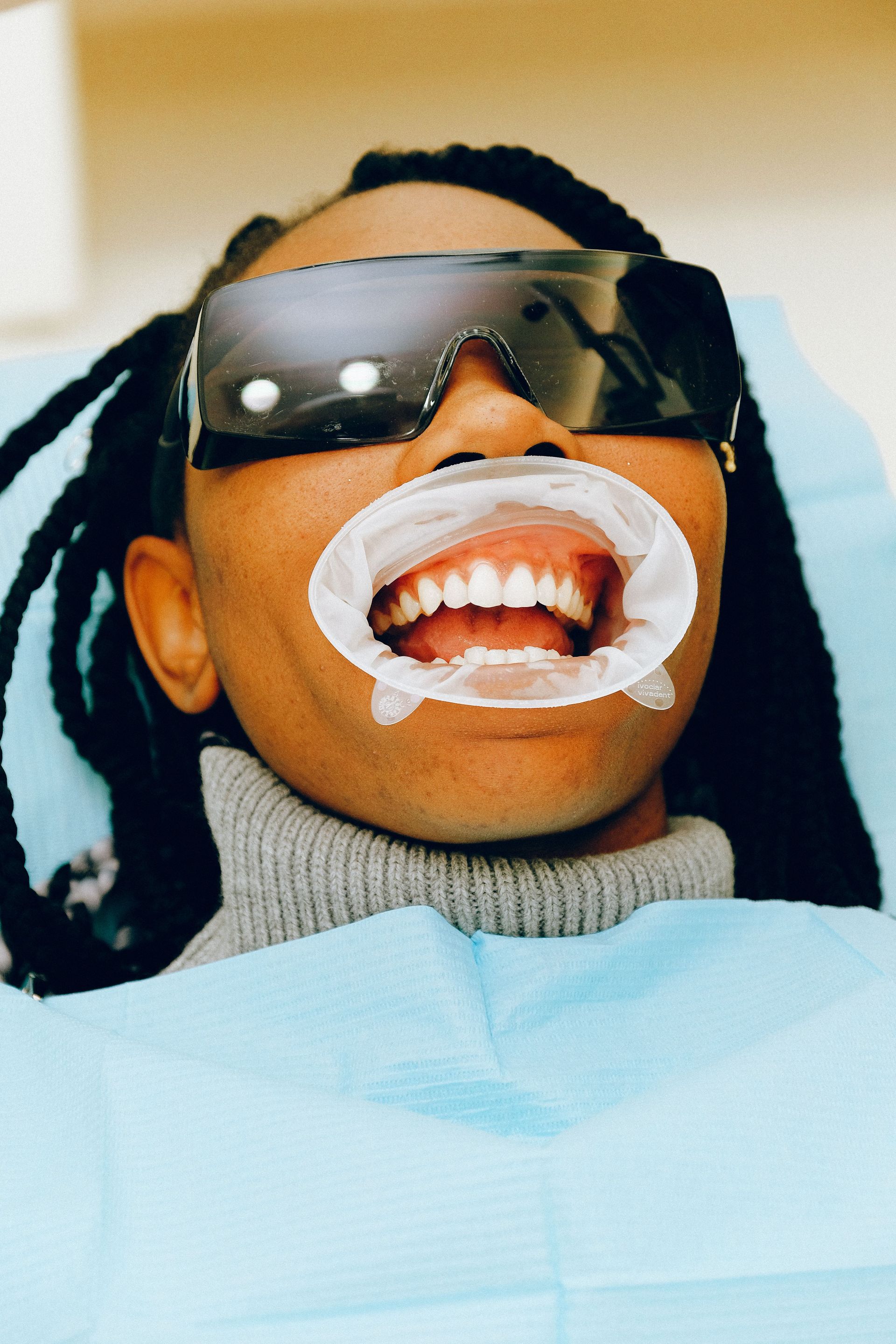 Person with sunglasses reclines in a dental chair, mouth open with white dental treatment material.