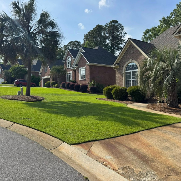 Suburban brick homes with manicured green lawns along a curved street on a sunny day