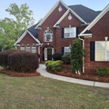 Brick suburban house with dark roof, white trim, arched windows, and a front lawn with shrubs.