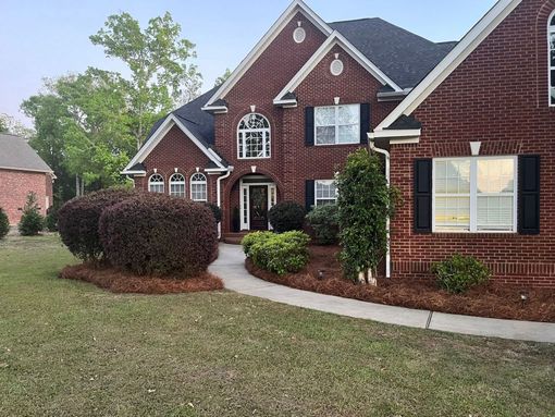 Brick suburban house with white trim, dark roof, and a curved walkway in a landscaped yard