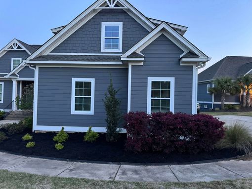 Gray house with white trim, front windows, and landscaped yard along a curved sidewalk.