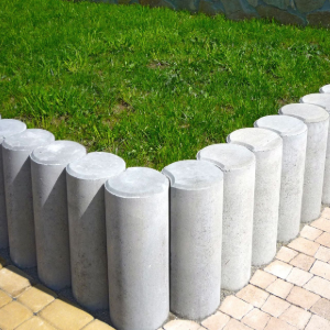 Short gray cylindrical bollards bordering a green lawn beside a brick walkway