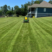 Lawn mower cutting a striped green lawn beside a blue house on a sunny day