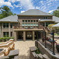 Backyard patio with brick house, balcony, stone seating area, and poolside fence under a blue sky