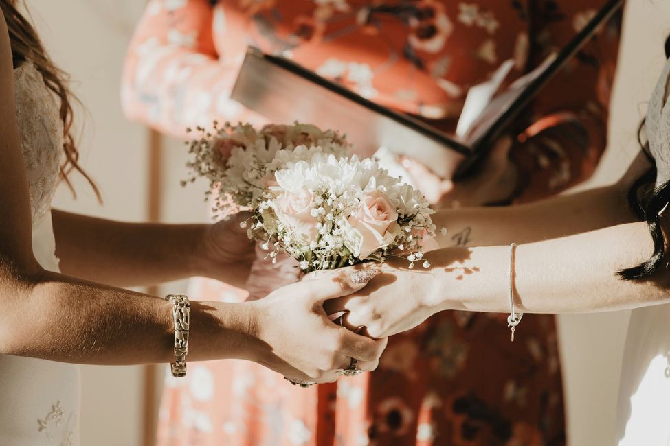Two people holding hands, a bouquet in between, during a ceremony.