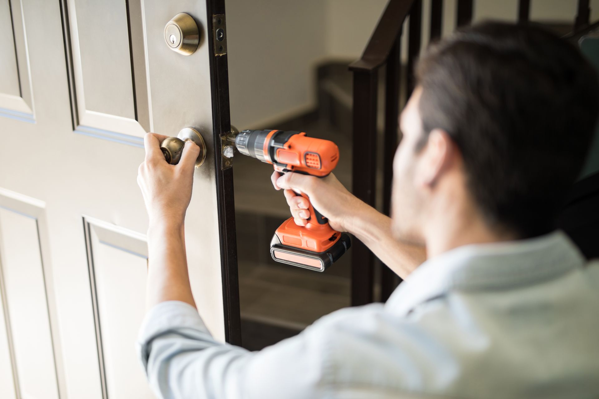 Person using a cordless drill to install a deadbolt lock on a white door