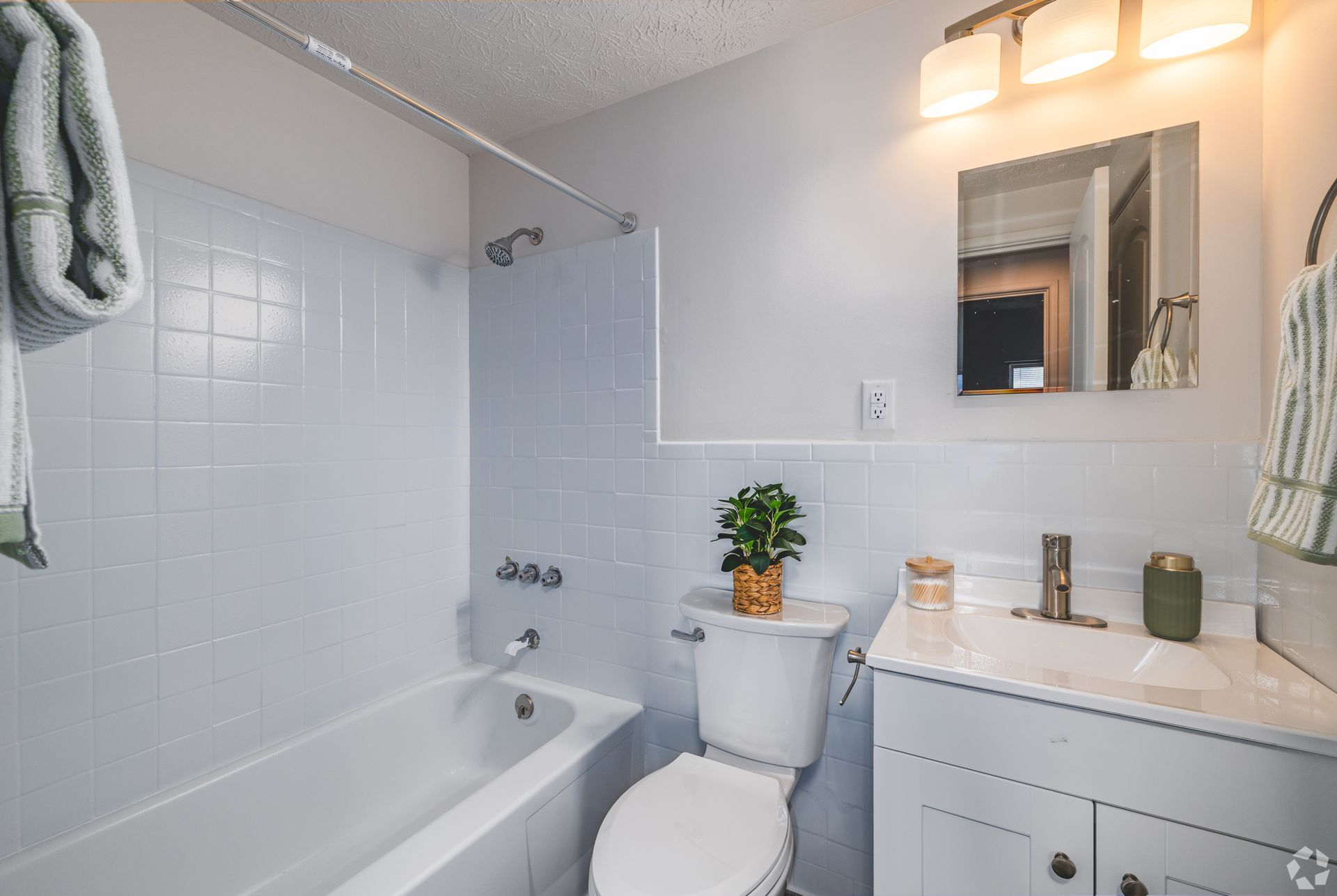 Updated bathroom at Overlook at Sunset with bathtub, vanity, mirror, and white tile shower surround.