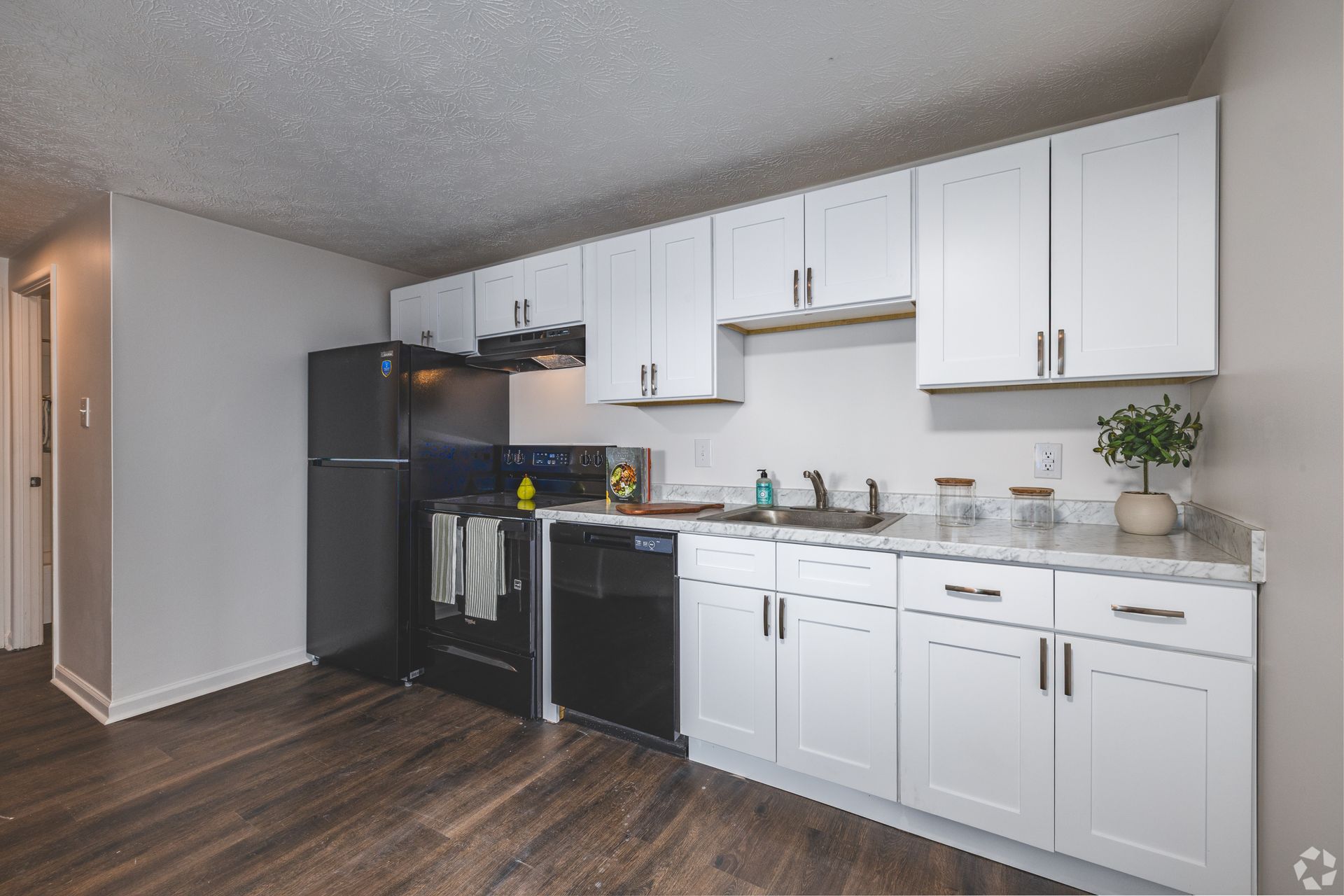 Updated apartment kitchen at Overlook at Sunset with white cabinets, black appliances, and wood-style flooring.