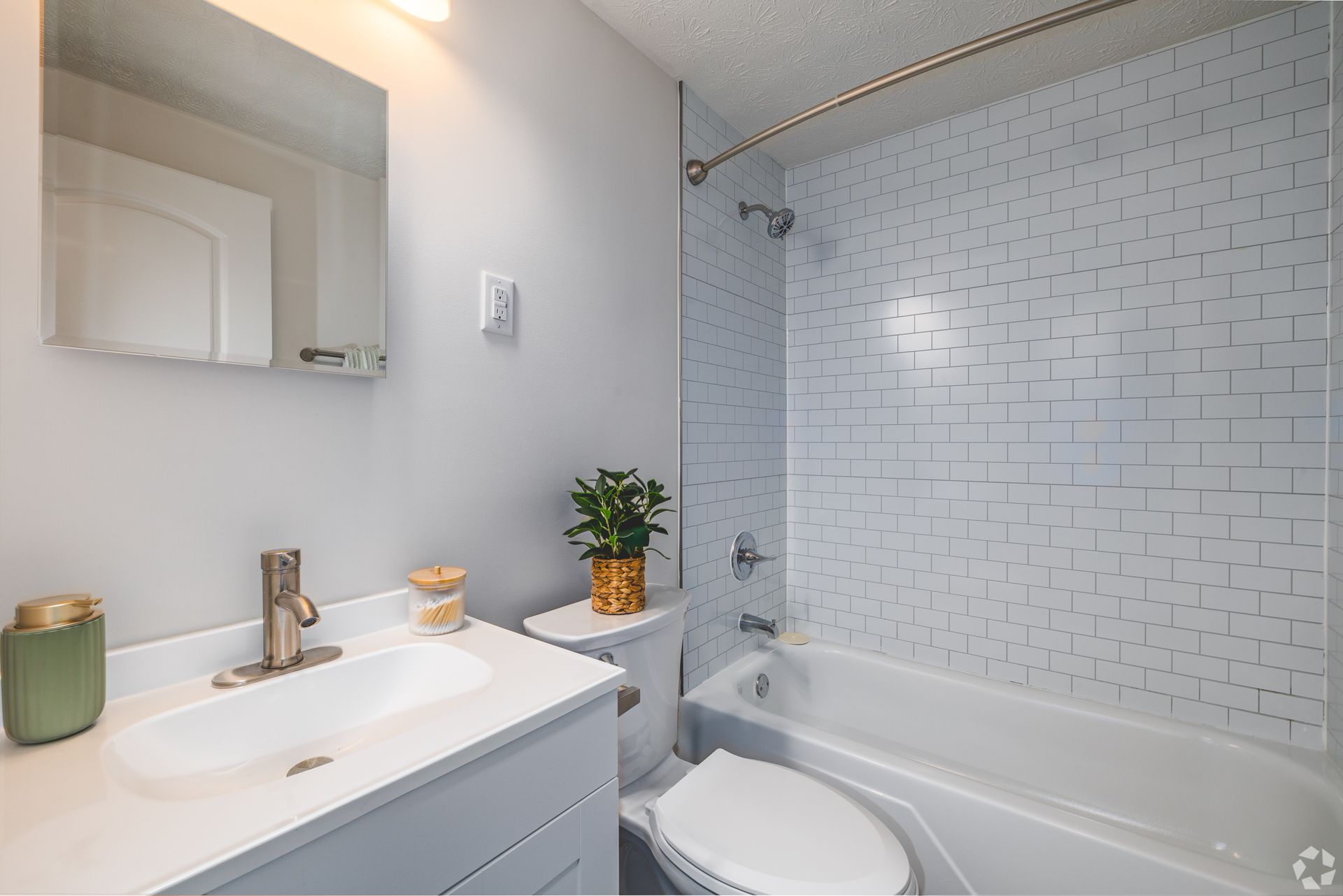 Updated bathroom at Overlook at Sunset with vanity, mirror, bathtub, and white tile shower surround.