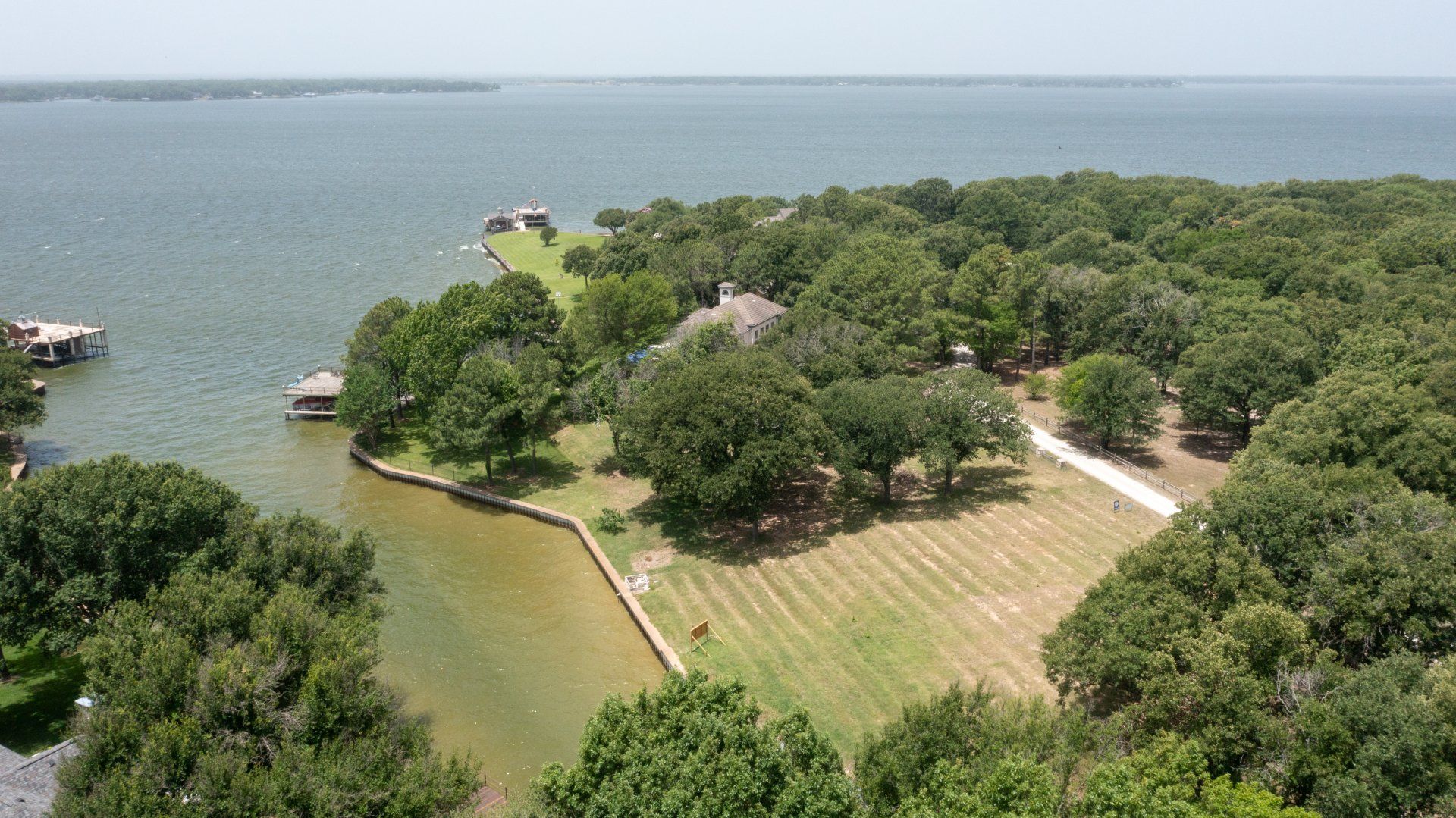 An aerial view of a house on a small island in the middle of a lake surrounded by trees.