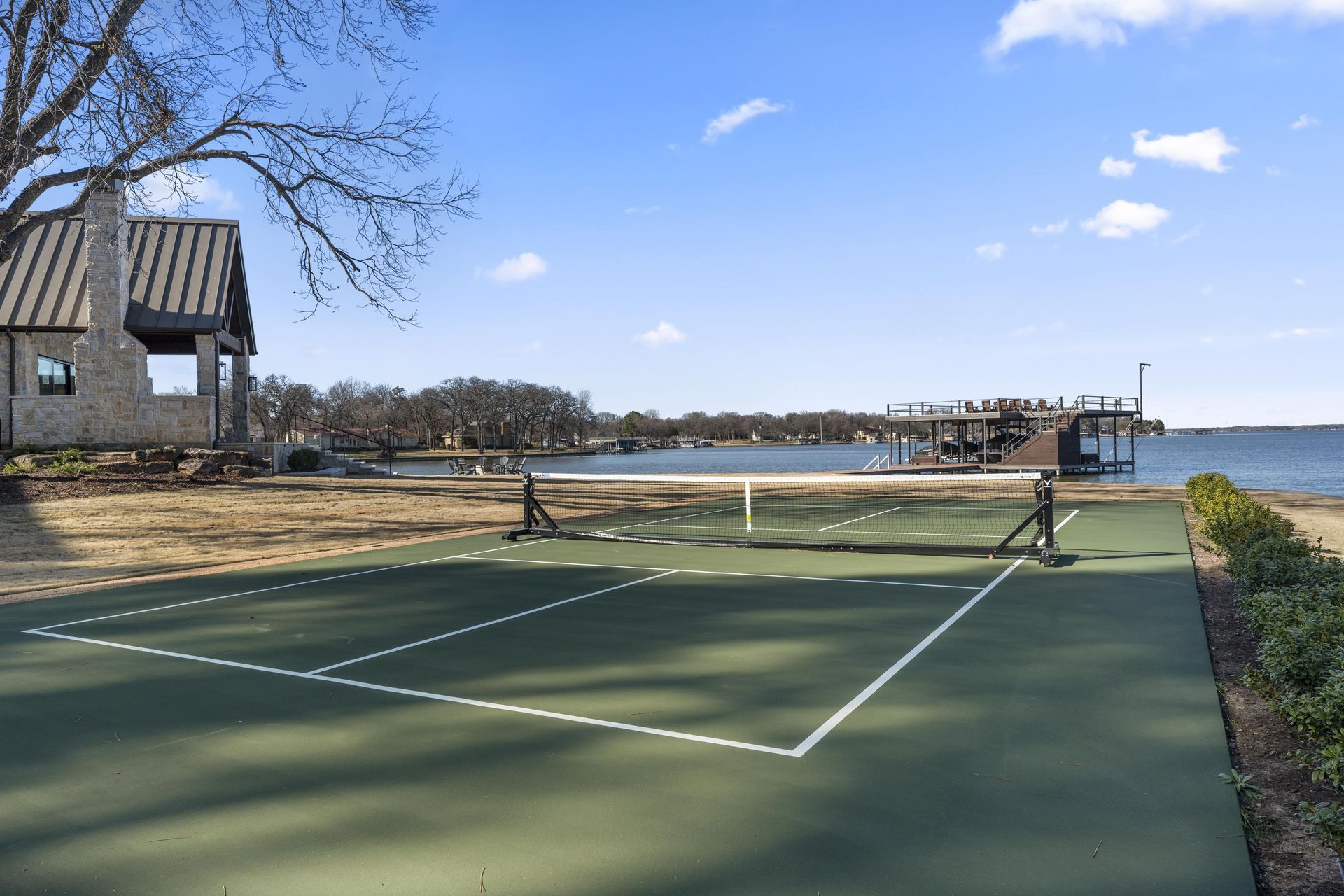 A tennis court next to a body of water with a house in the background.