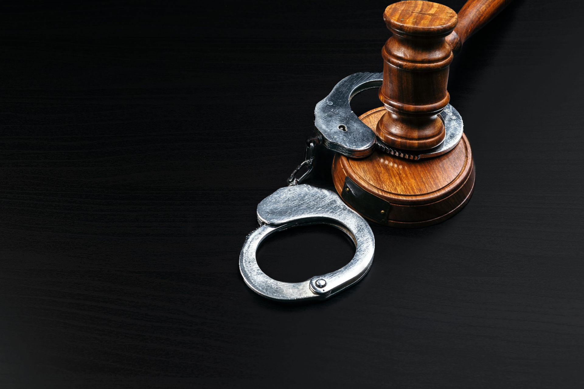 Handcuffs beside a judge’s gavel on a dark surface