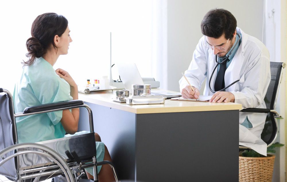 A Woman in a Wheelchair is Sitting at a Desk Talking to a Doctor — Mount Archer Medical Centre in Berserker, QLD