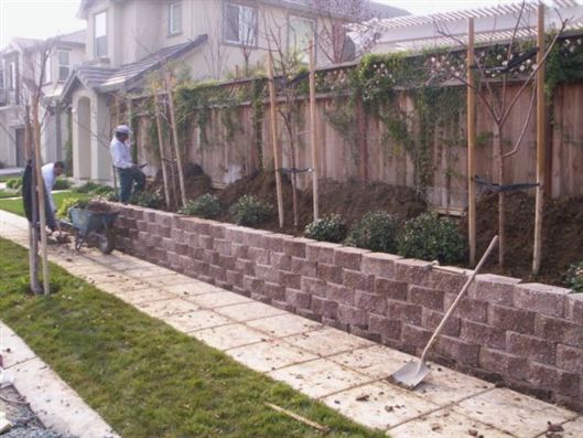 Two workers building a stone retaining wall beside a sidewalk and grassy yard
