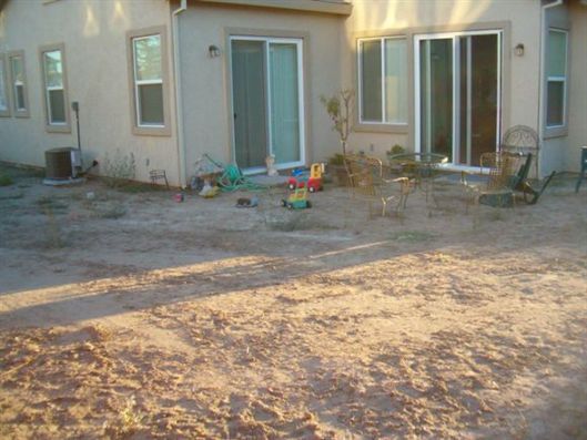 Backyard patio with sliding doors, dirt ground, and scattered children’s toys near a house