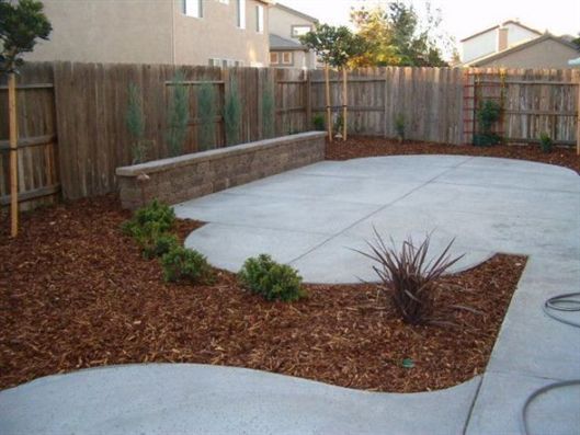 Backyard patio with concrete slabs, mulch beds, and a wooden fence围墙