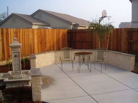 Backyard patio with concrete slab, small table and chairs, wooden fence, and stone fountain