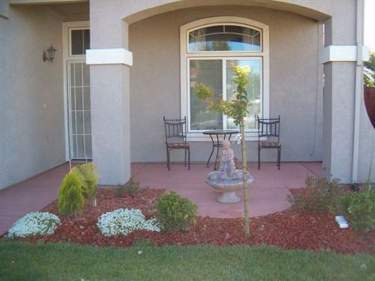 Front porch with two chairs, small table, and a potted plant beside a landscaped front yard.