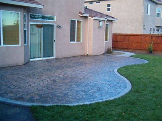 Backyard patio with stamped concrete, sliding glass doors, and a green lawn beside a fenced yard