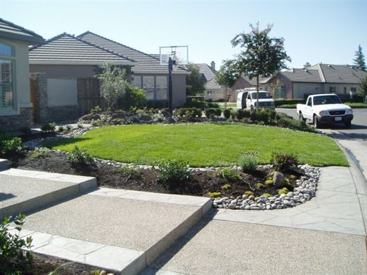 Front yard with circular green lawn, stone edging, driveway, and a white pickup truck in front of a house
