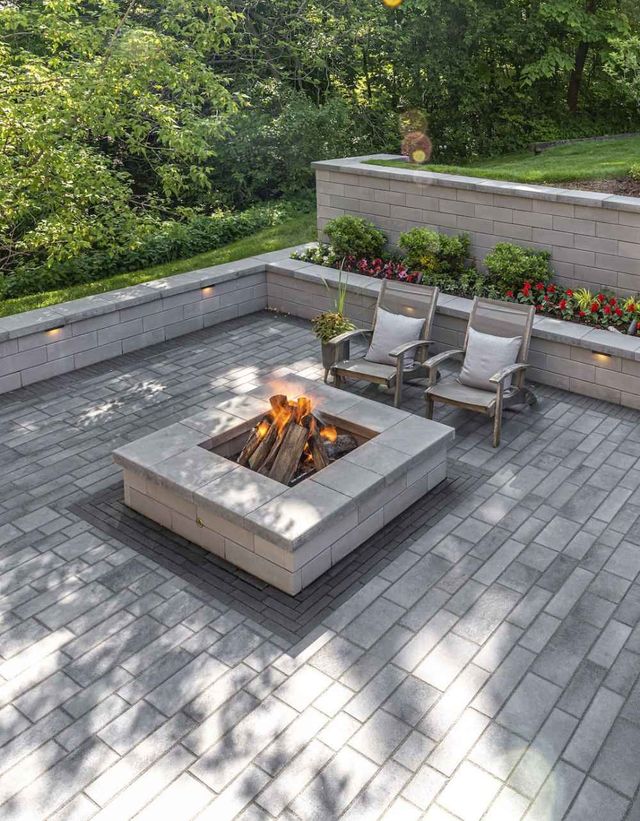 Modern backyard patio with a square fire pit, two lounge chairs, flower beds, and stone pavers