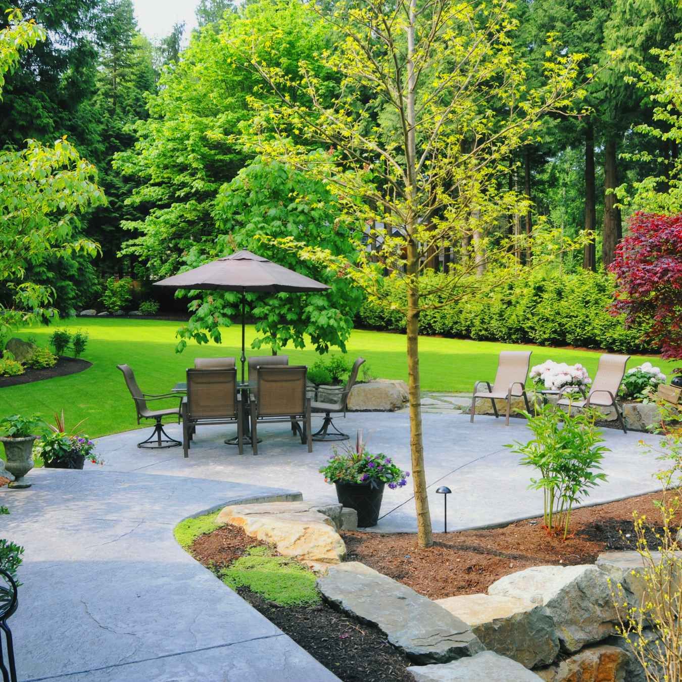 Landscaped patio with outdoor dining set, umbrella, lounge chairs, and lush green garden