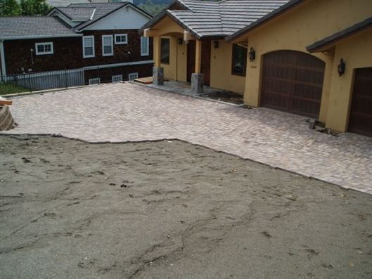 Newly paved driveway and walkway beside tan houses, with wet sand in the foreground.
