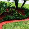 Curved red flower bed with lush green plants and palm trees in a landscaped garden