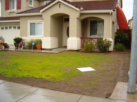 Suburban house with a small front yard, wet pavement, and a white stepping stone near the lawn.