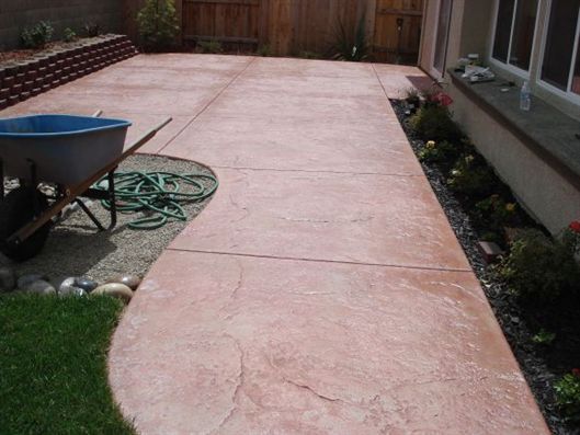 Backyard patio with stamped concrete, a hose, and a small planter bed beside a house