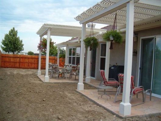 Patio with white pergola, outdoor seating, and a dry dirt yard beside a house