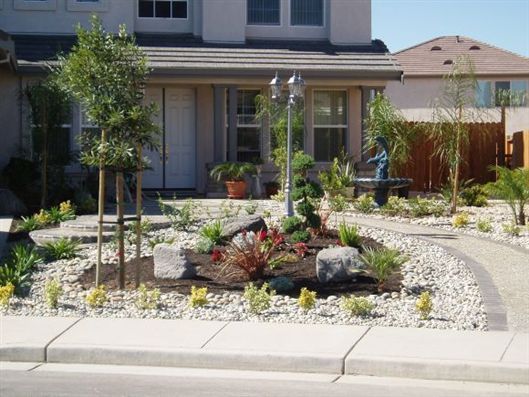 Front yard desert garden with rocks, shrubs, and a curved stone path beside a house