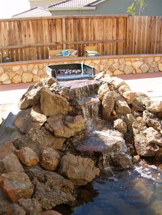 Rock waterfall feature in a backyard pond with stone steps and flowing water